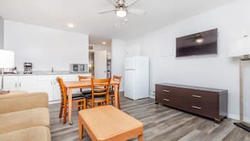 Una cocina moderna con armarios blancos, un comedor con una mesa y sillas de madera, un mueble de madera oscura y un ventilador de techo.