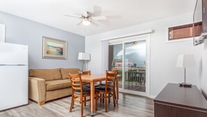 A modern kitchen with a white refrigerator, wooden dining table, and chairs. There is a beige sofa and a ceiling fan. - Westridge Motor Inn (Osoyoos)