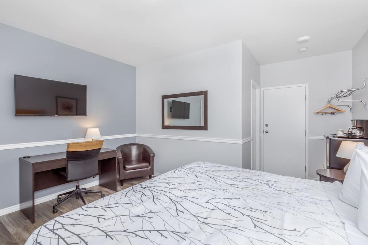 A hotel room with a bed, a desk, a chair, a TV, and a wardrobe.