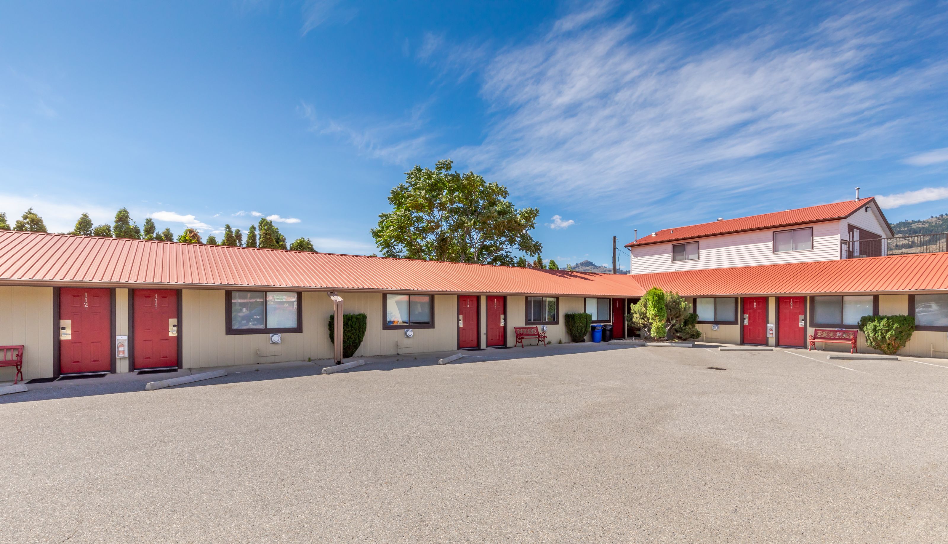 Un motel con varias puertas rojas, un estacionamiento y un cielo azul despejado.