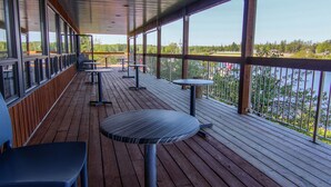 Una terraza techada al aire libre con suelo de madera, barandillas de metal y mesas y sillas.