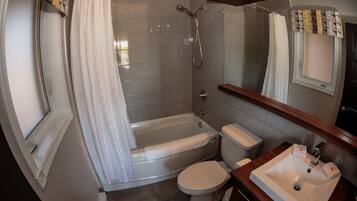 Un baño moderno con ducha envuelta en vidrio, inodoro y lavamanos con espejo.