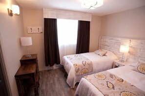 Habitación de hotel con dos camas, un escritorio, una lámpara y un ventanal con cortinas.