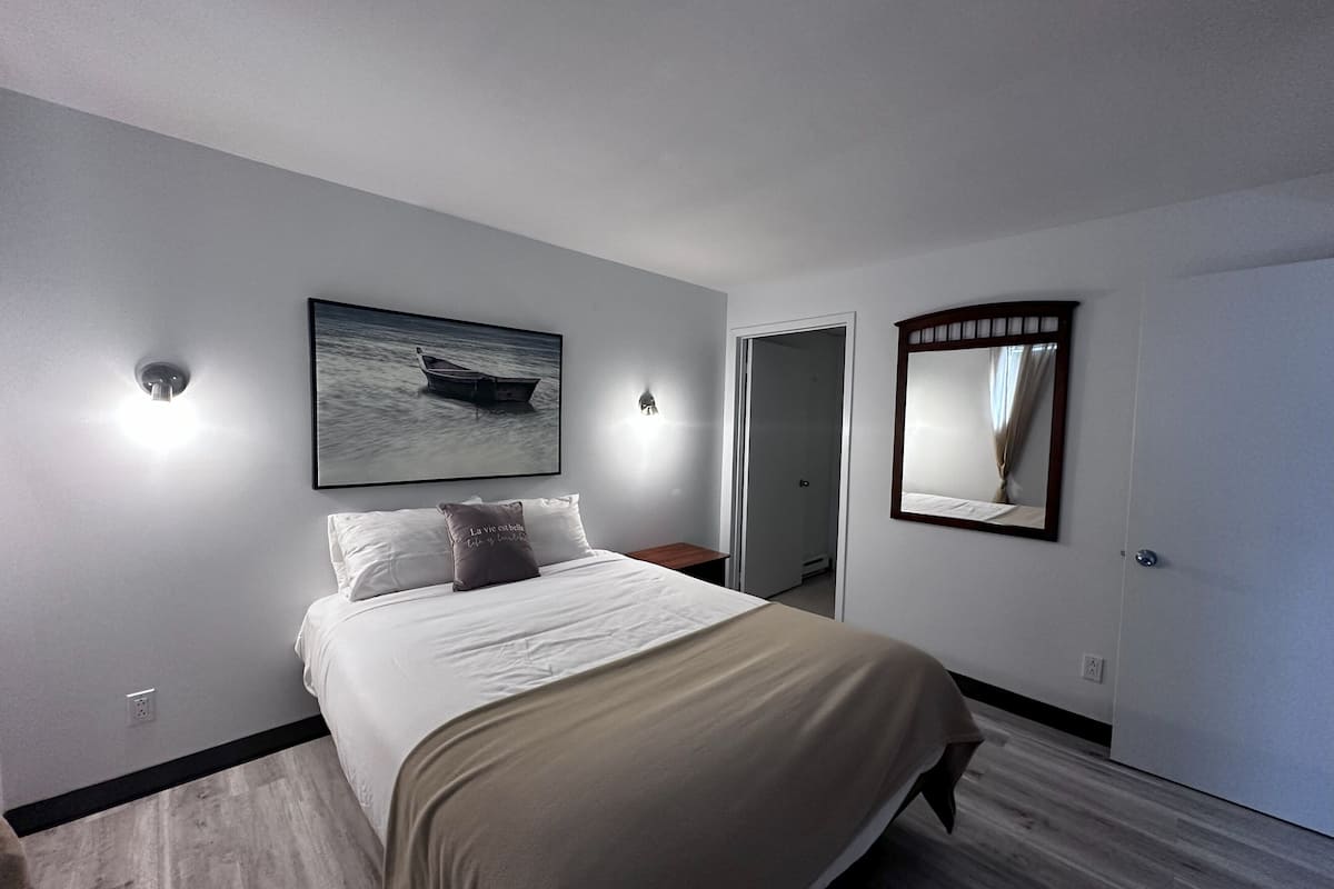 A bedroom with a bed, a painting of a boat, a mirror, and a door.