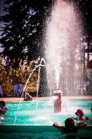 Una piscina con una fuente de agua, rodeada de gente disfrutando.