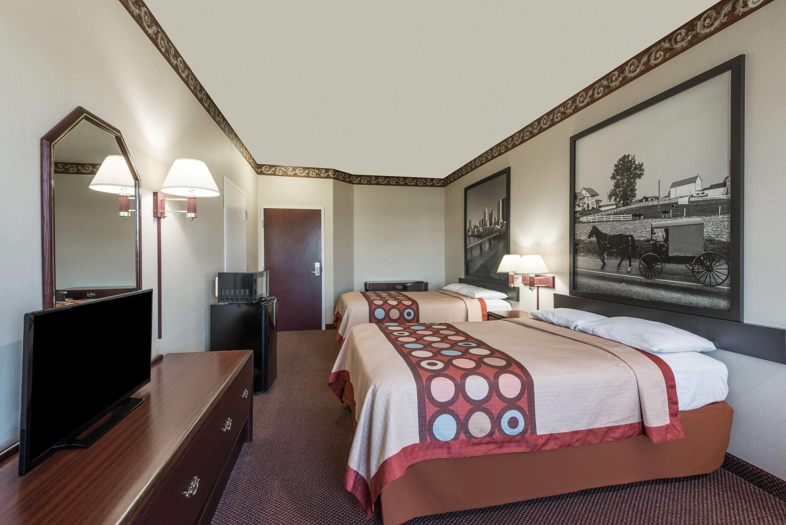 Habitación de hotel con dos camas, un televisor, un escritorio y un cuadro grande en la pared.