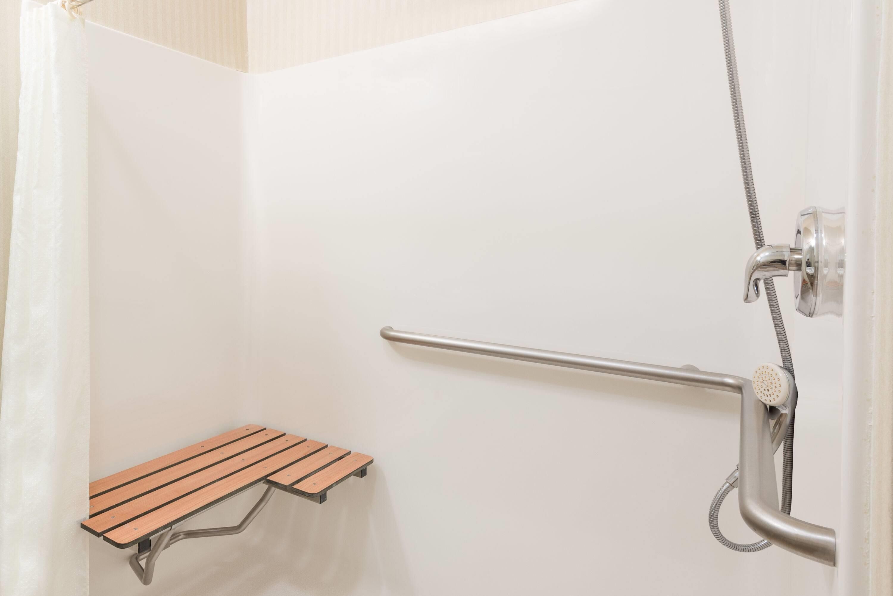 A shower area with a grab bar, a wooden bench, and a showerhead.