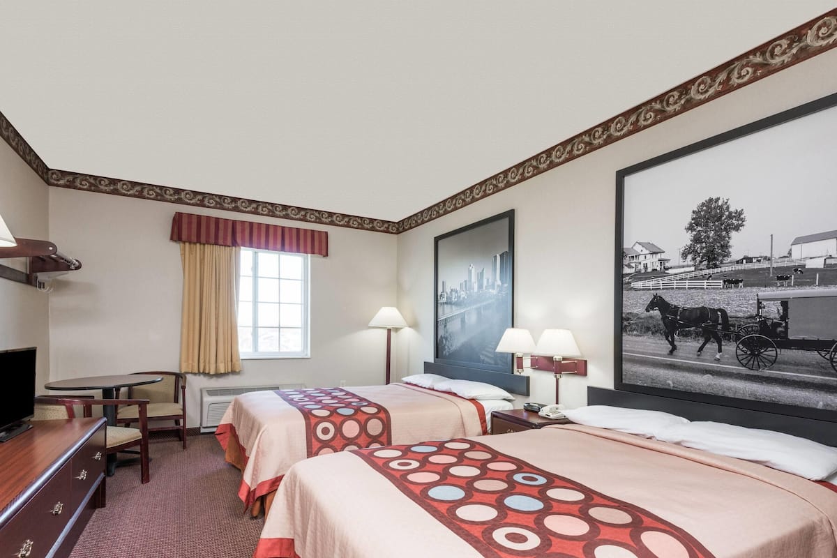 A hotel room with two beds, a desk, a television, and a large framed picture on the wall.