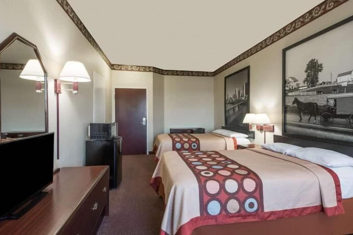 A hotel room with two beds, a TV, a desk, and a mirror.