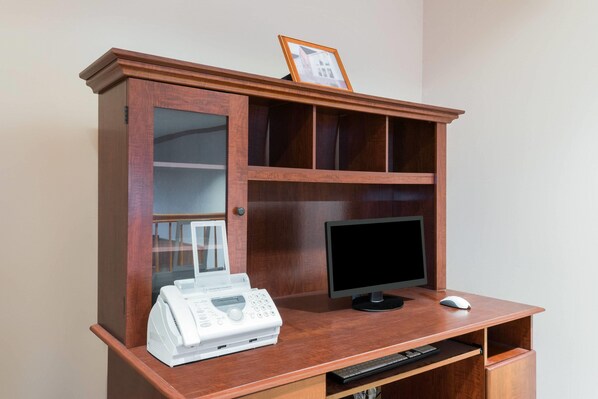 Un escritorio de madera con un monitor de computadora, una impresora y un marco con una fotografía.