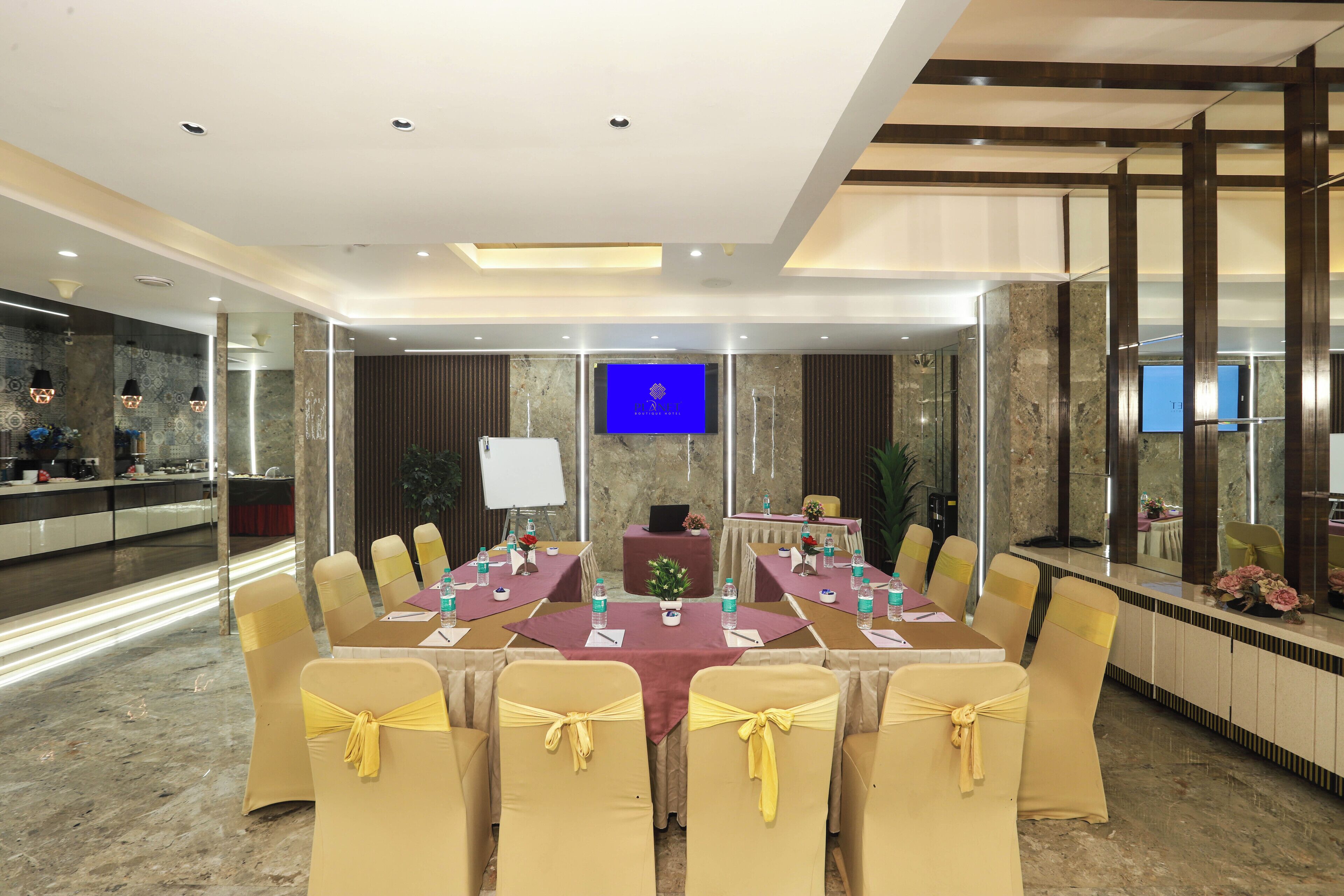 Un salón de conferencias con una larga mesa, sillas con cintas amarillas, una pantalla de televisión y una pared de mármol.