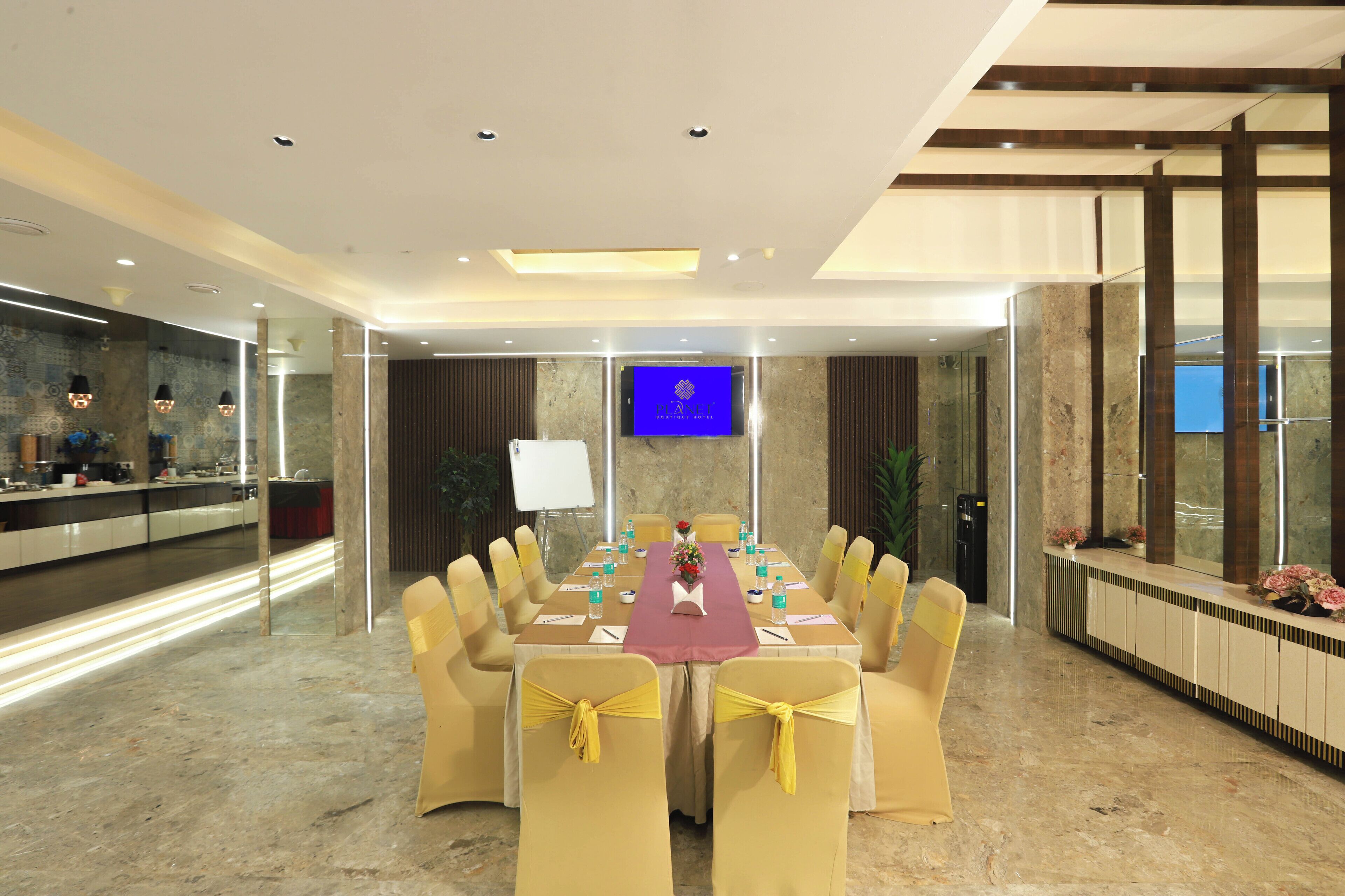 A conference room with a long table, yellow chairs, and a TV screen.