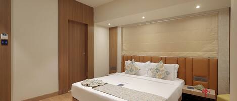 A modern hotel room with a large bed, a bedside table, a nightstand, a wooden wardrobe, and a ceiling light.