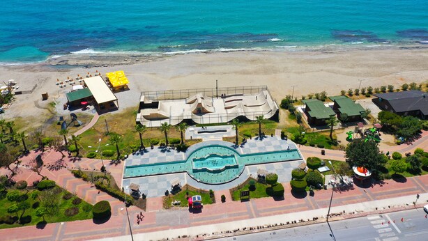 Vista aèria d'una estació turística a la costa, amb una piscina central, serveis a la platja i una zona de pàrquing.