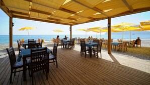 Un restaurant a la vora de la platja amb terrassa, taules de fusta i paraigües grocs.