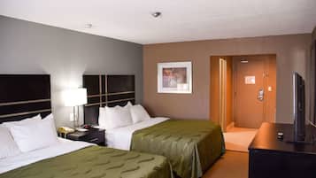 A hotel room with two beds, a desk with a lamp, a television, and a door to the bathroom.