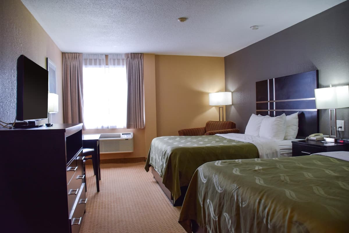 A hotel room with two beds, a desk, a TV, and a window with curtains.