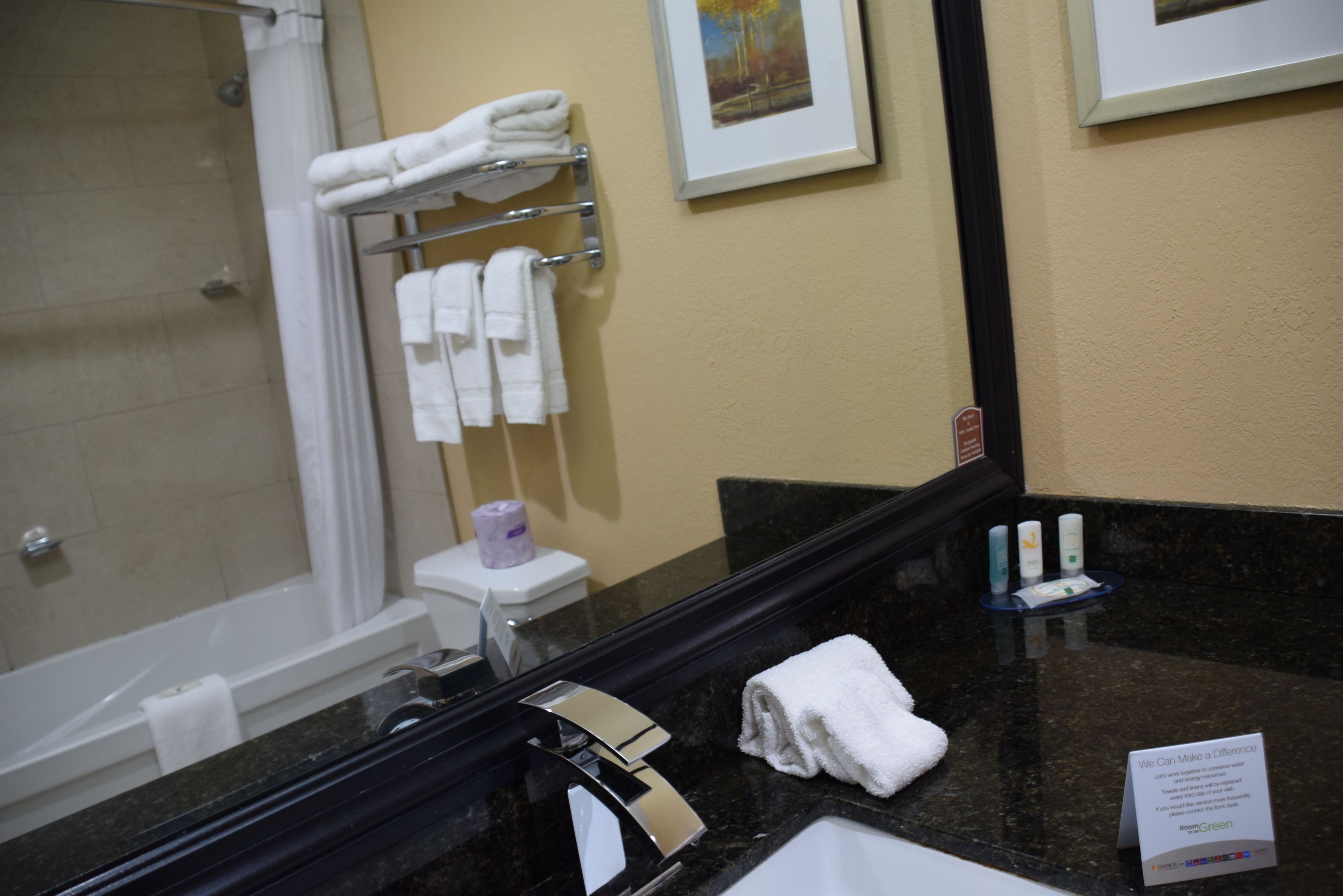 A bathroom with a bathtub, a toilet, a towel rack with towels, a sink with toiletries, and a framed picture on the wall.