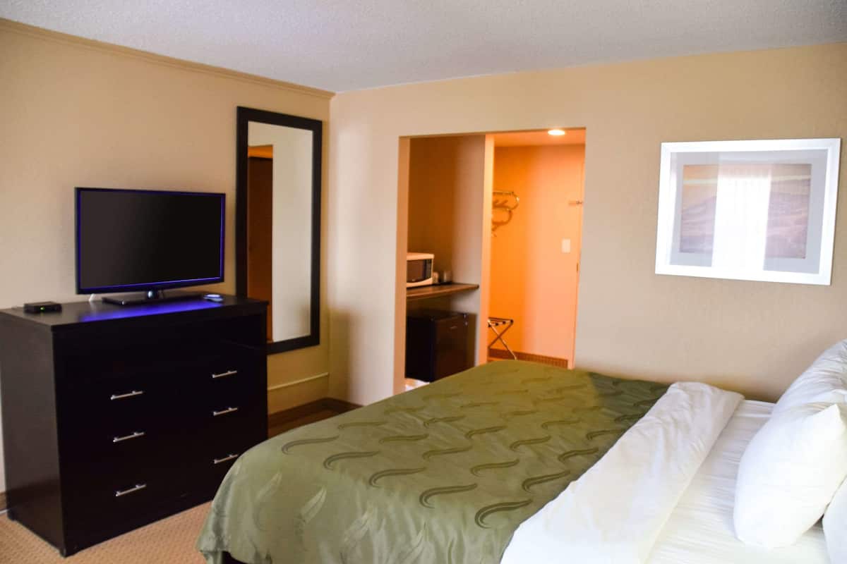 A bedroom with a bed, a dresser, a television on the dresser, a framed picture on the wall, and a doorway leading to a bathroom.