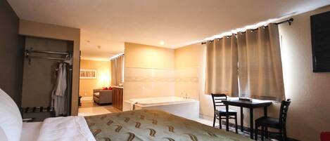 A hotel room with a bed, a bathroom with a bathtub, a table with chairs, and a desk.