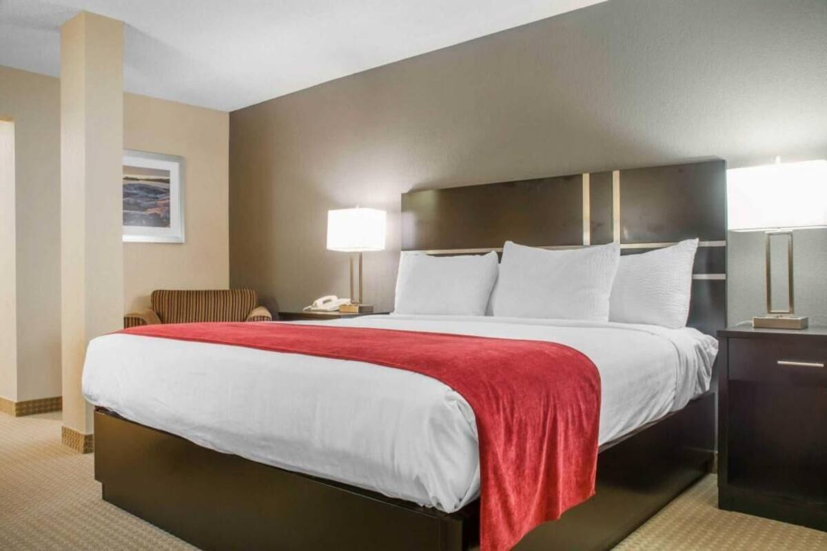 A hotel room with a bed, bedside tables, a lamp, a chair, and a painting on the wall.