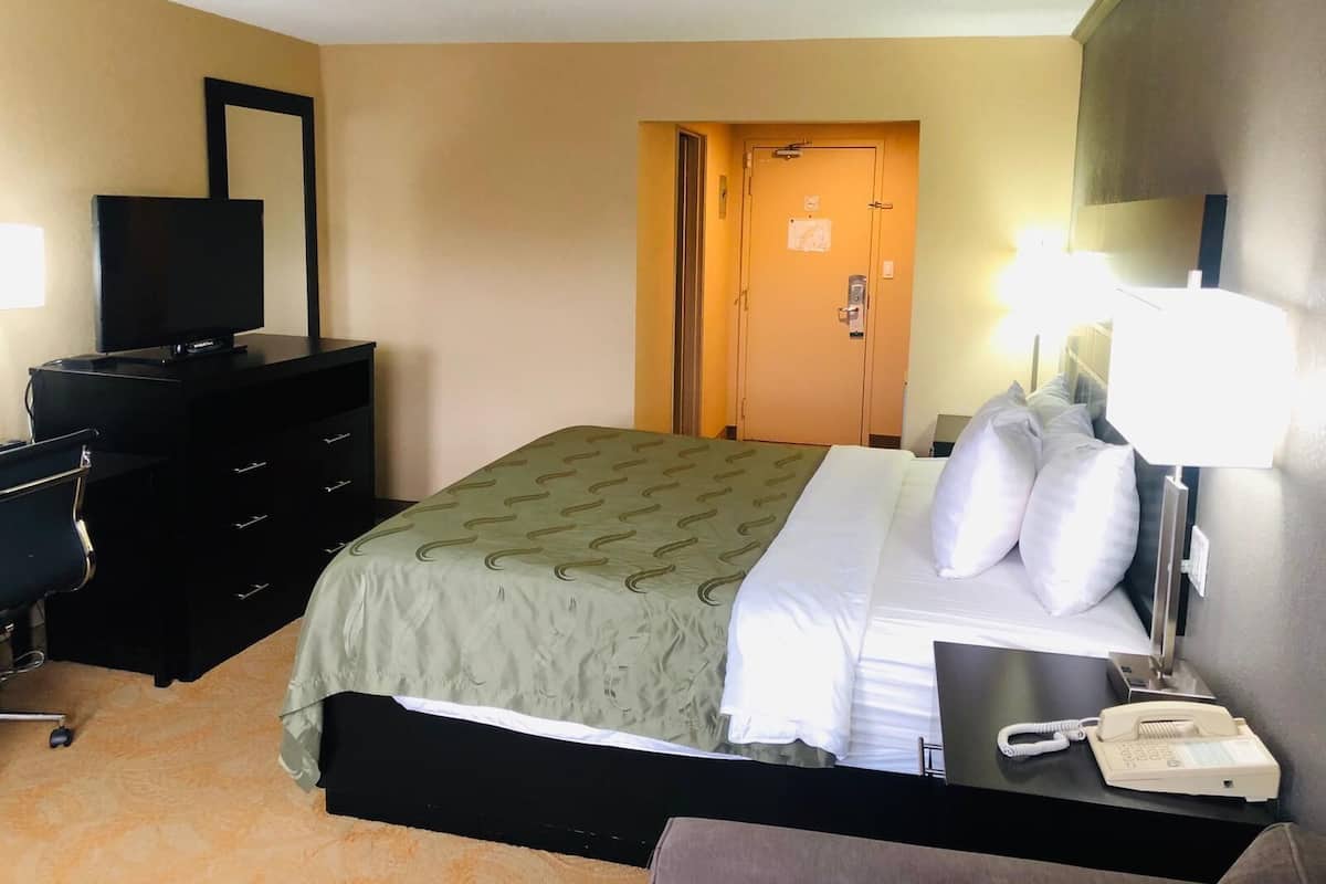 A hotel room with a bed, a desk with a telephone, a television, a dresser, and a door.