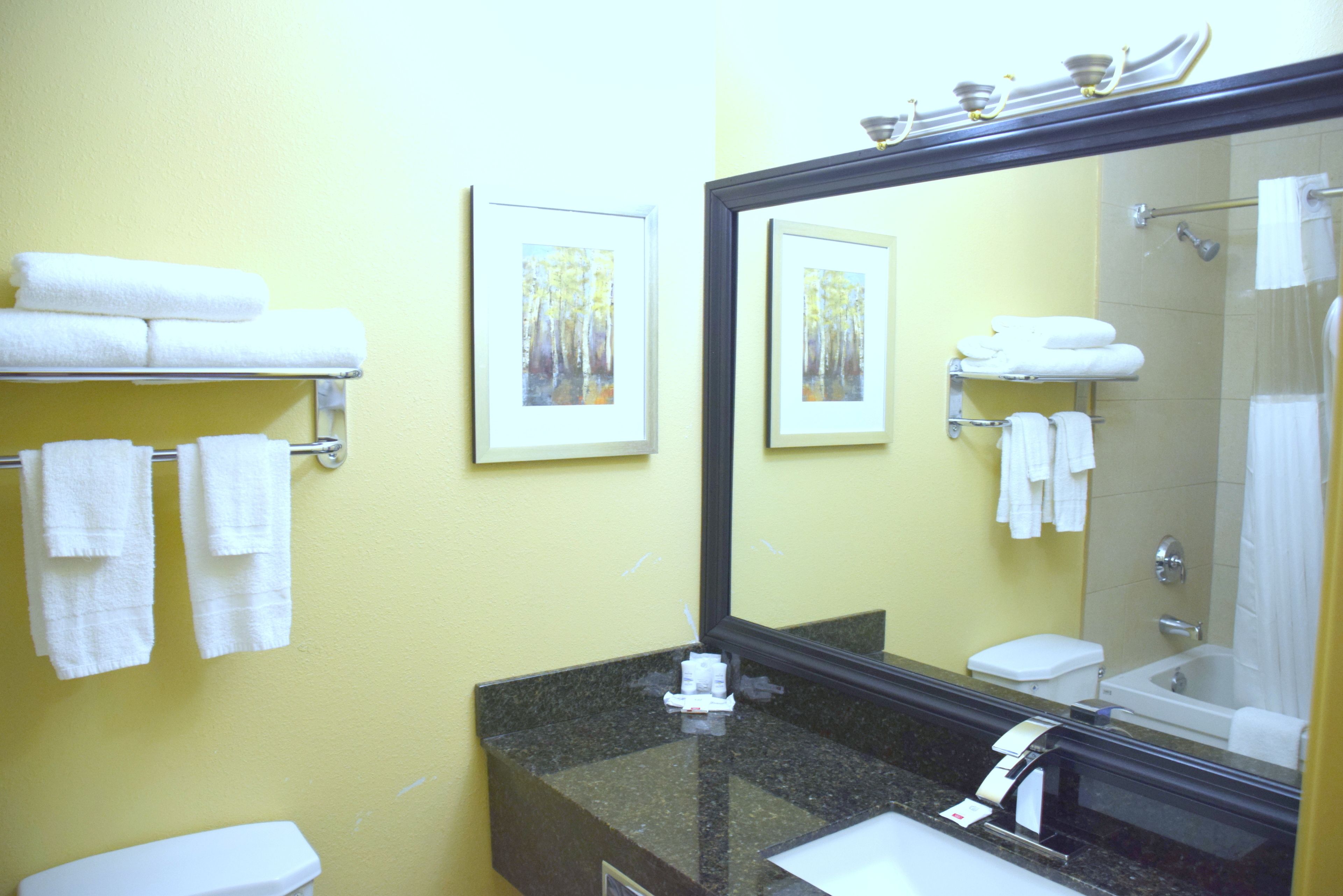 A bathroom with a yellow wall, a black granite sink, a white toilet, and a bathtub. There are white towels on a rack and a framed picture on the wall.