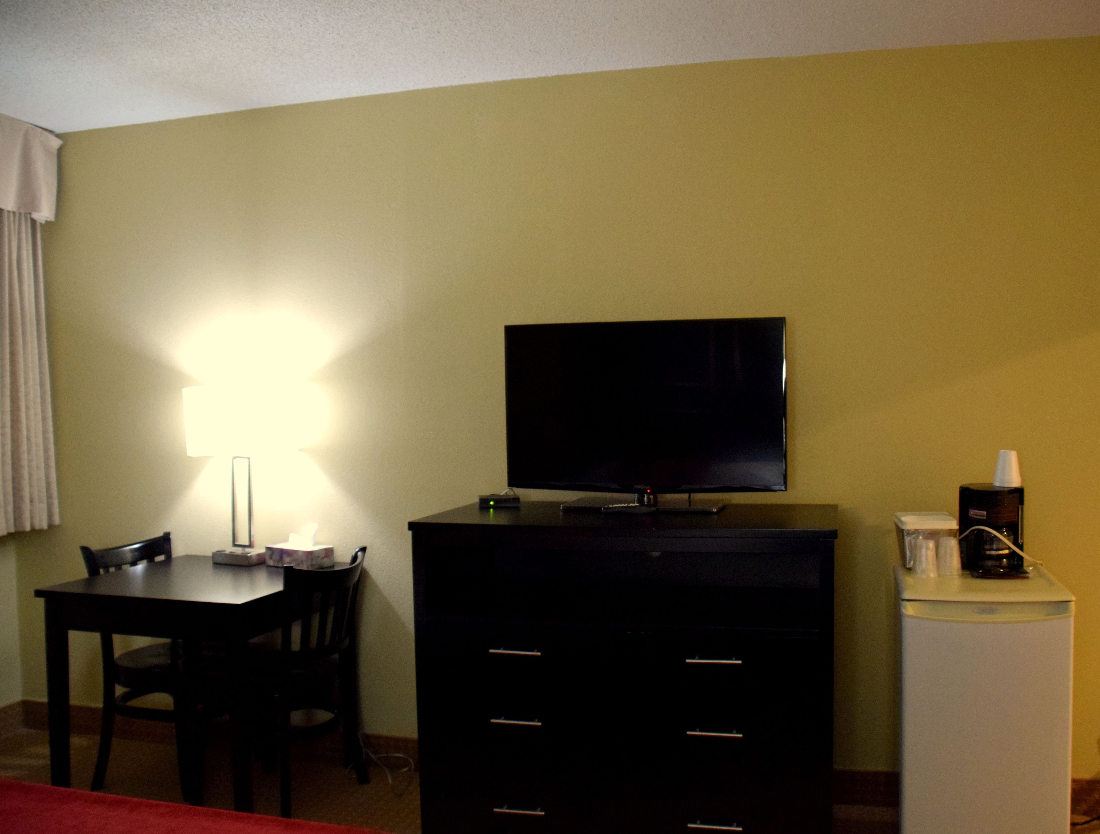 A hotel room with a television on a cabinet, a desk with a chair, and a small refrigerator.