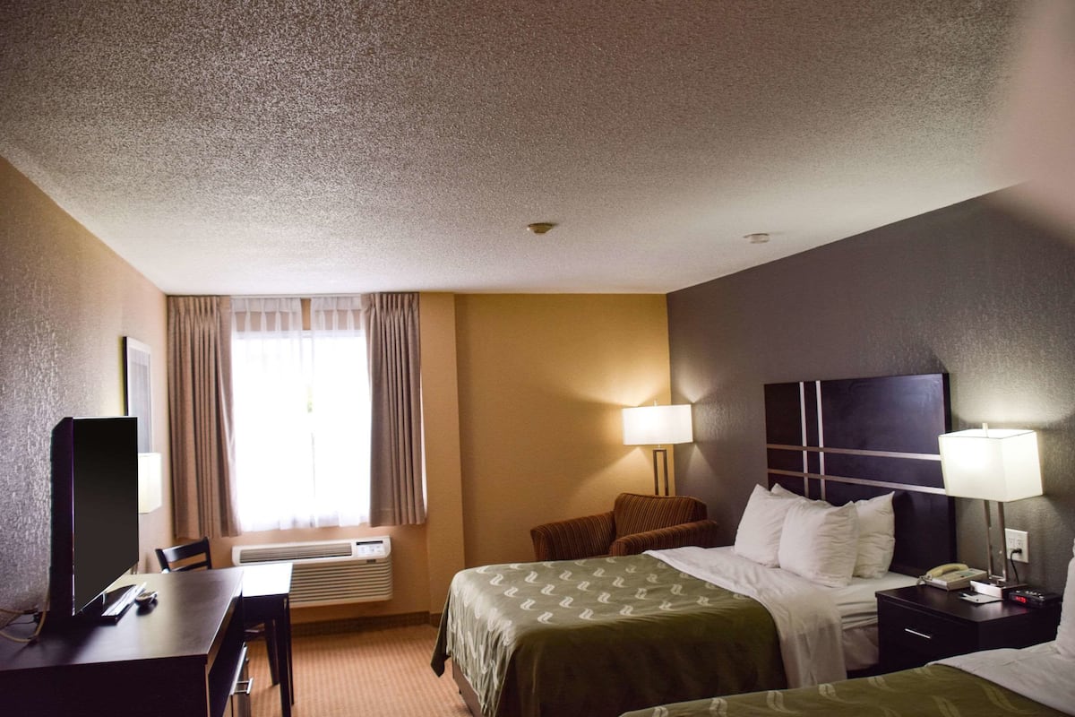 A hotel room with a bed, a desk, a chair, a TV, and a window with curtains.