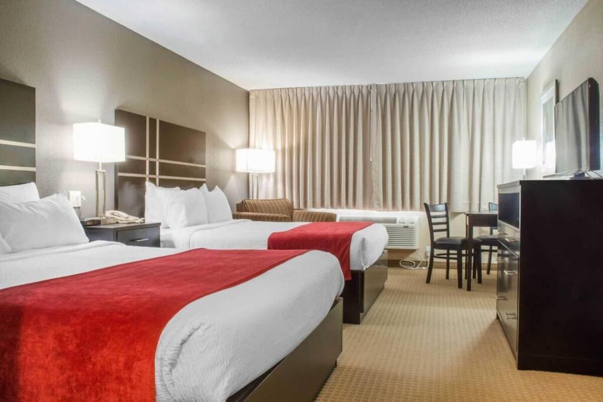 A hotel room with two beds, a desk, a chair, a television, and a minibar.