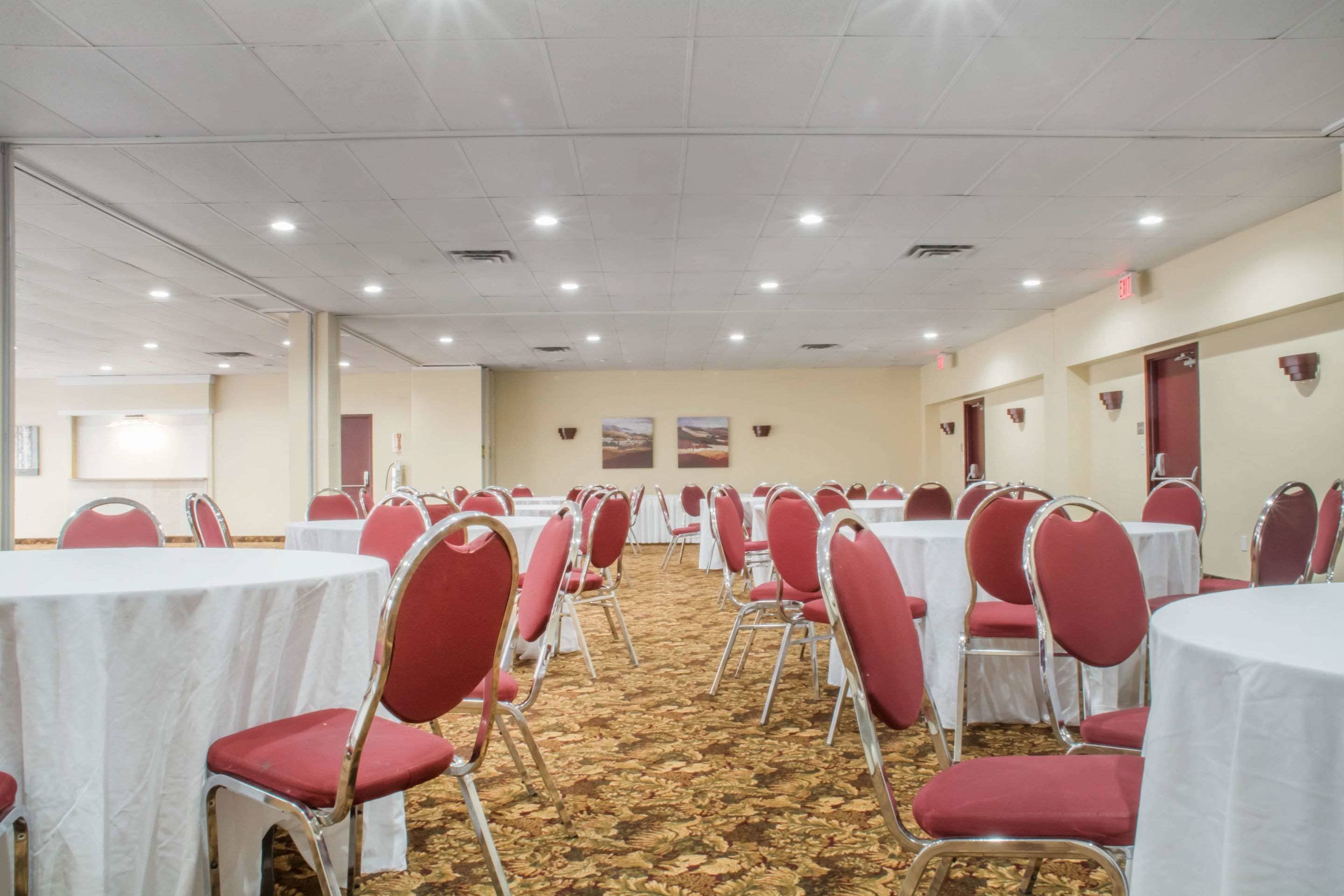 A conference room with rows of tables and chairs, carpeted floor, and ceiling lights.