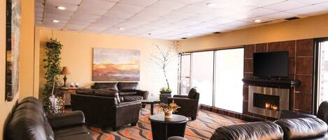 A spacious lounge with leather sofas, a flat-screen TV, a fireplace, and large windows.