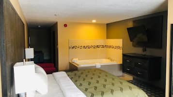 Habitación de hotel con cama, baño con bañera, televisor y una silla roja.