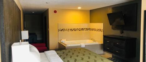 A hotel room with a bed, a bathroom with a bathtub, a TV, and a red chair.