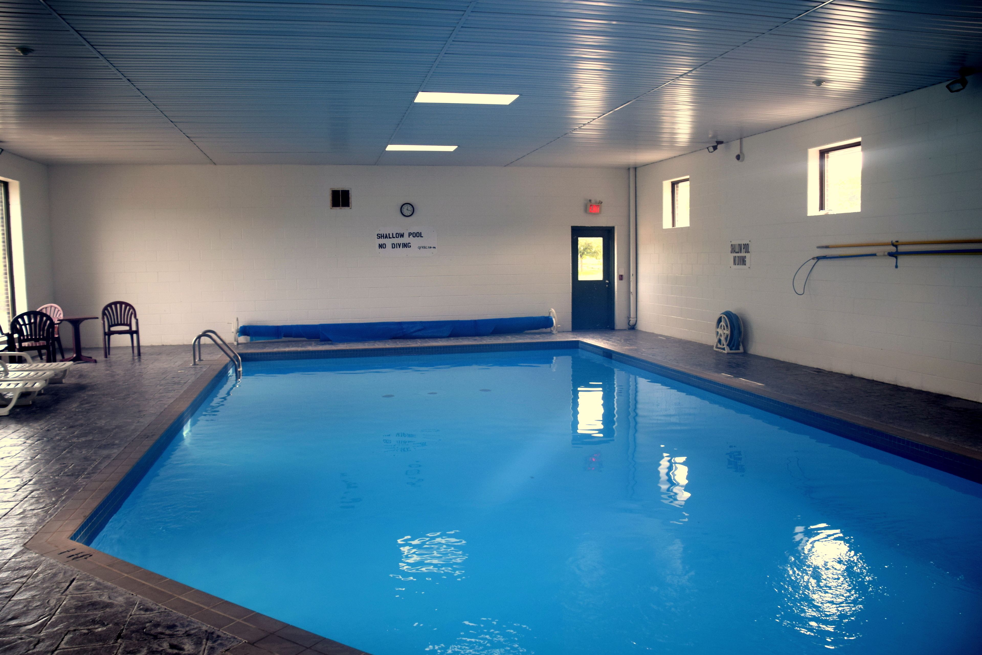 Une piscine intérieure avec un panneau indiquant qu’il est interdit de plonger, une horloge et une porte.