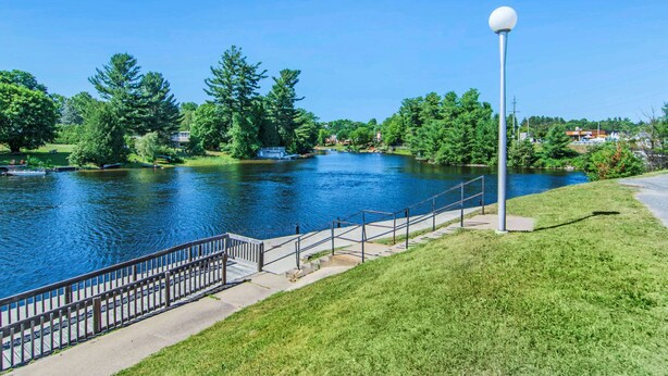 A riverside walkway with a metal railing, a lamp post, and a grassy area.