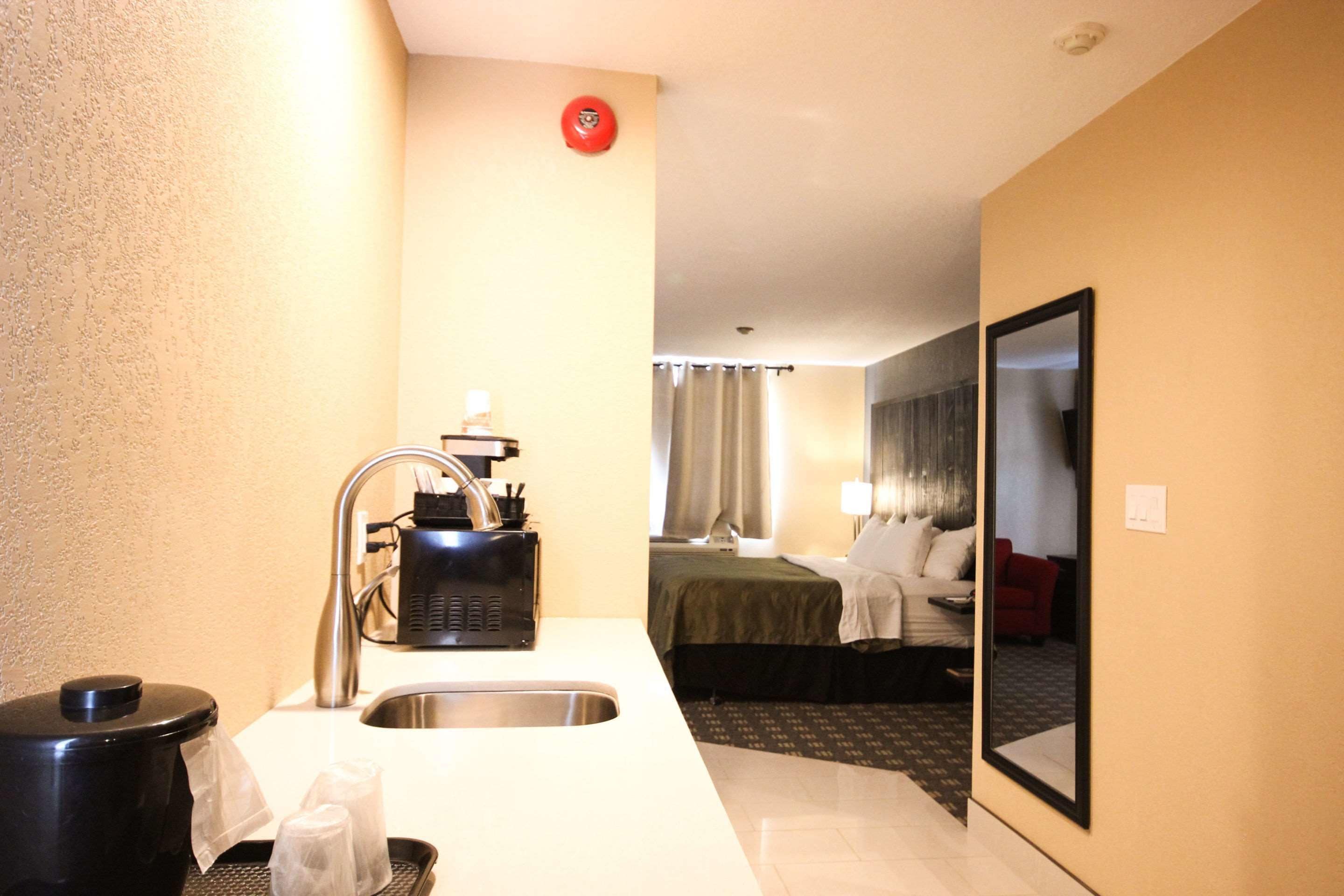A compact hotel room with a kitchenette, a bed, and a mirror.