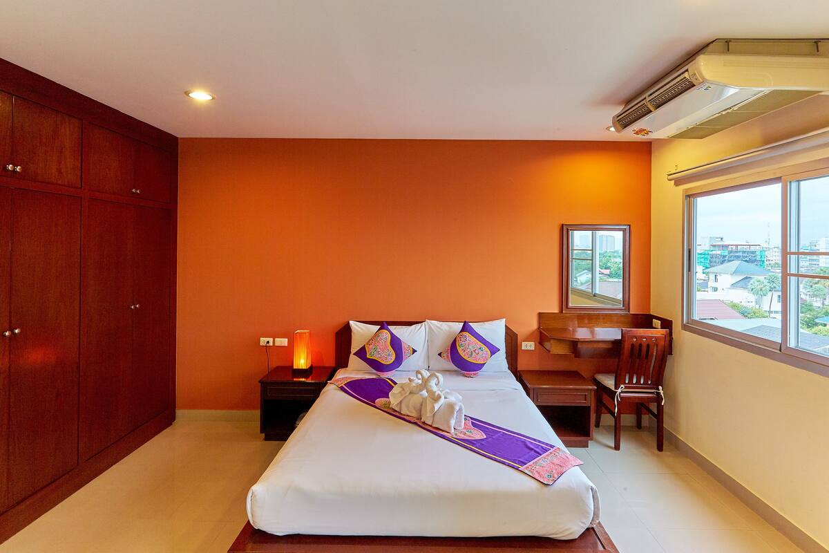 Habitación de hotel con una cama grande, paredes color naranja, un escritorio y vistas a edificios fuera de la ventana.
