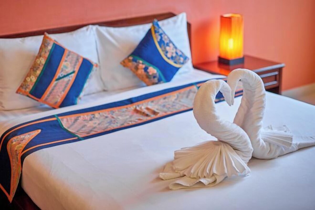 A bed with a decorative swan towel arrangement and a patterned bedspread.