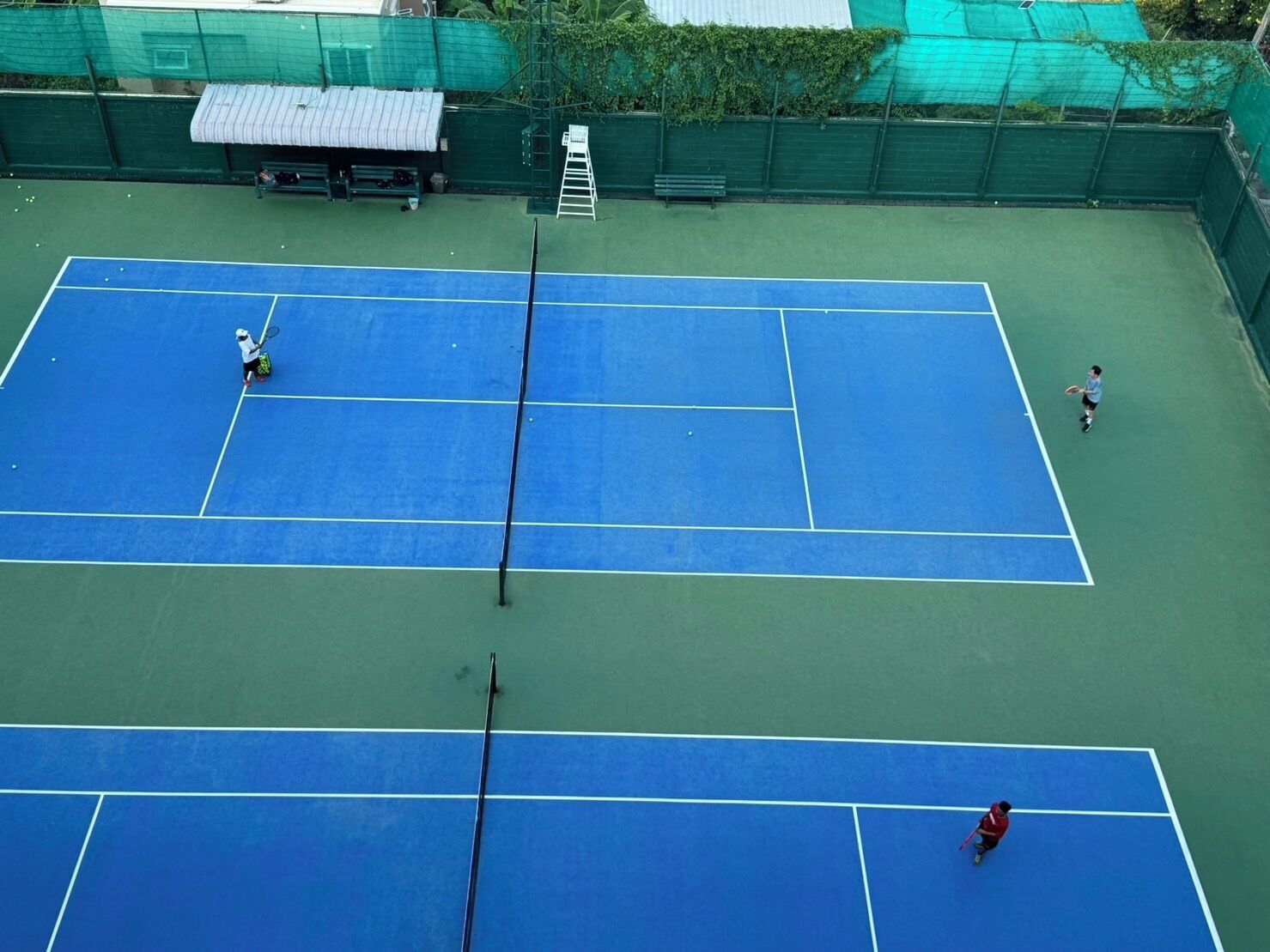 Een tennisbaan met een net in het midden, omgeven door een groene hekken.
