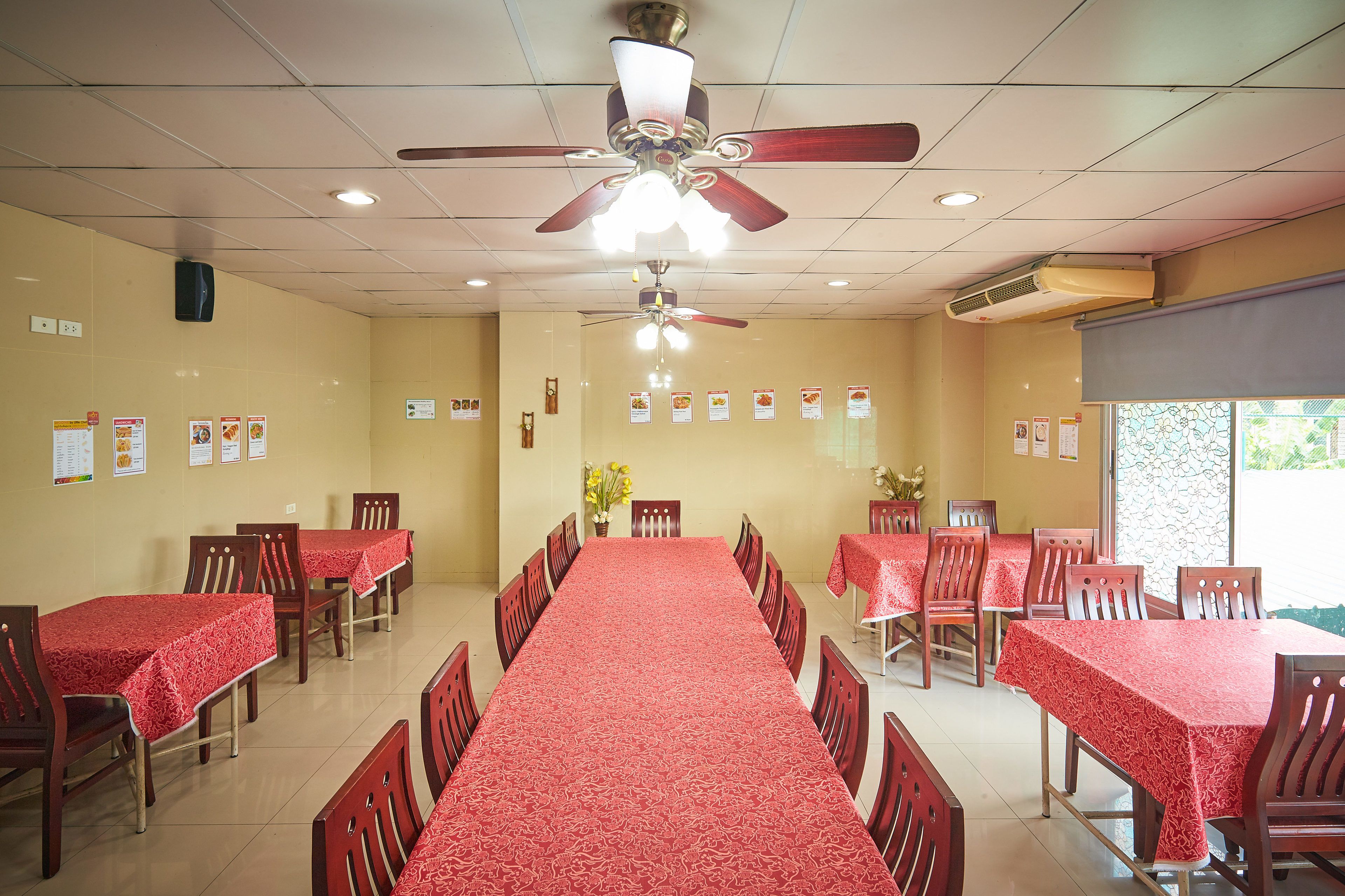 Une salle de conférence avec une longue table, des chaises, des ventilateurs de plafond et des éléments décoratifs sur les murs.
