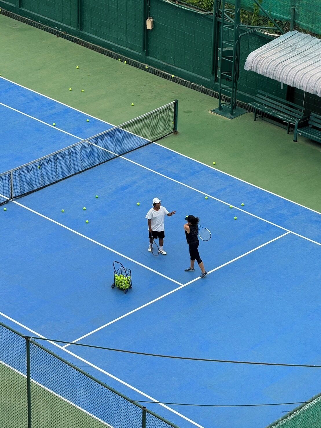 Una cancha de tenis con una red, una valla verde y un banco.