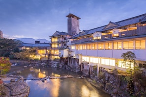 A traditional Japanese ryokan with multiple buildings, a stone bridge, and a river. - Wataya Besso (Ureshino)