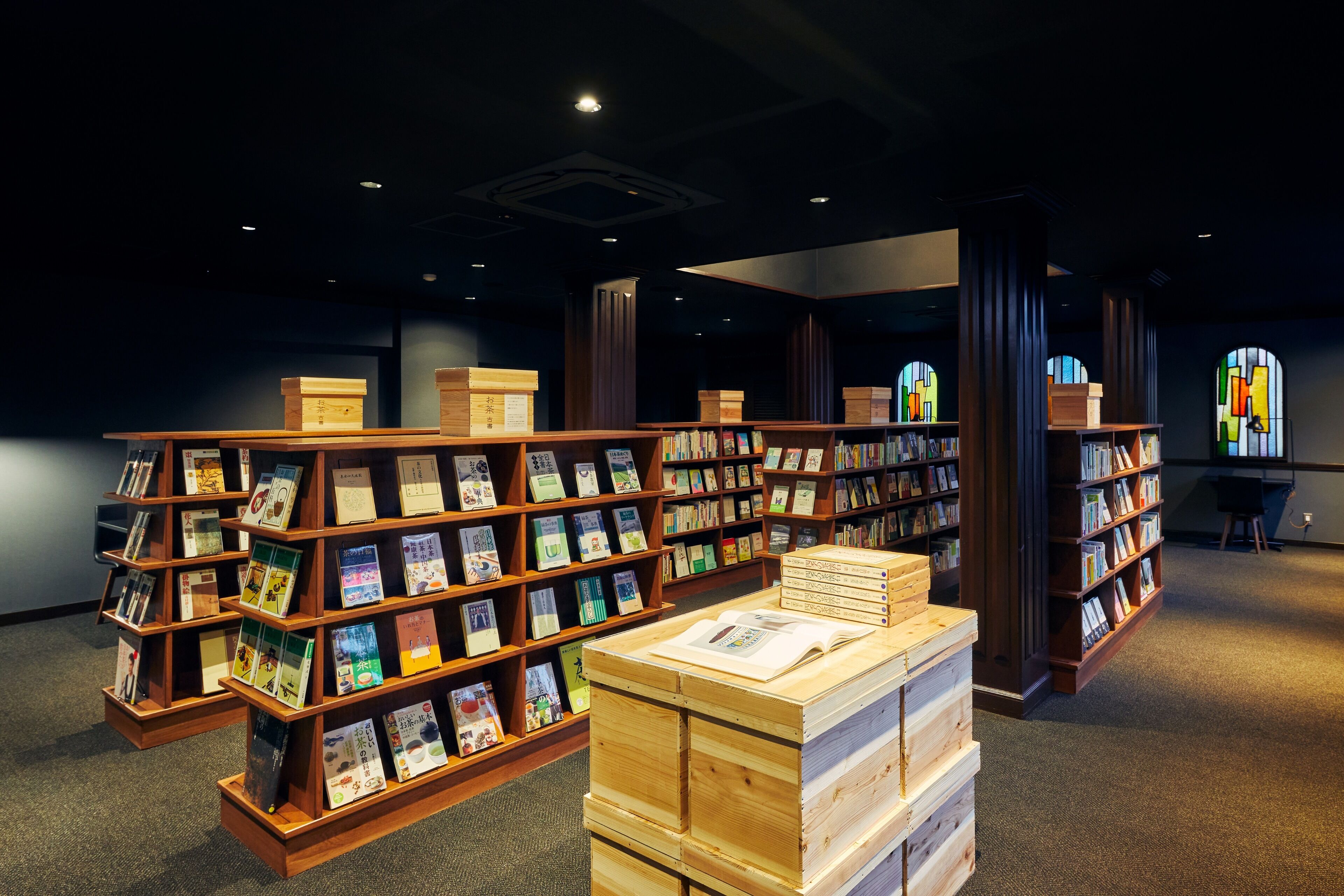 A library with wooden bookshelves filled with books and a stack of books on a table.