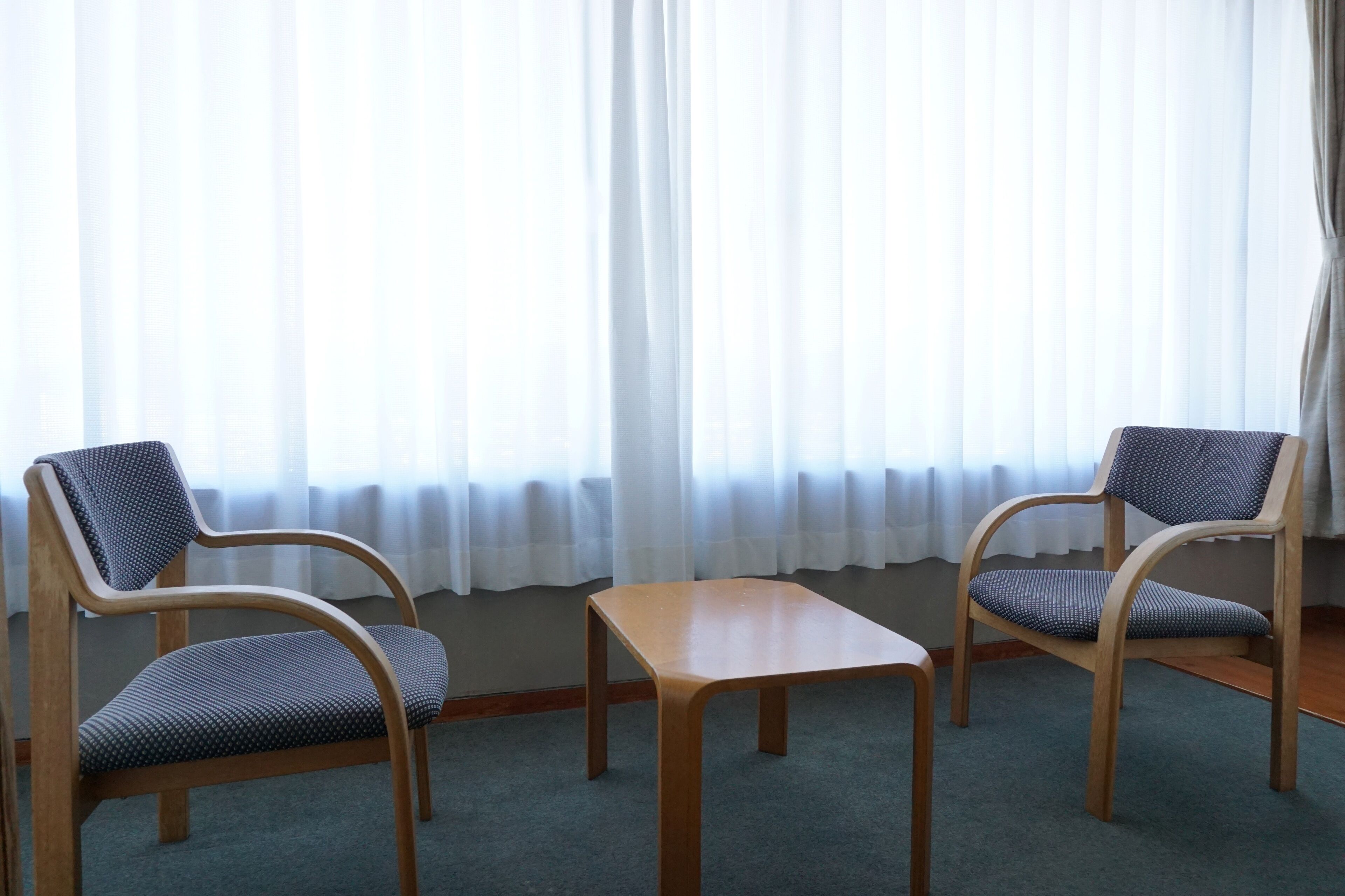 Una habitación con dos sillas de madera con cojines azules, una mesa de madera y una ventana con cortinas de gasa.
