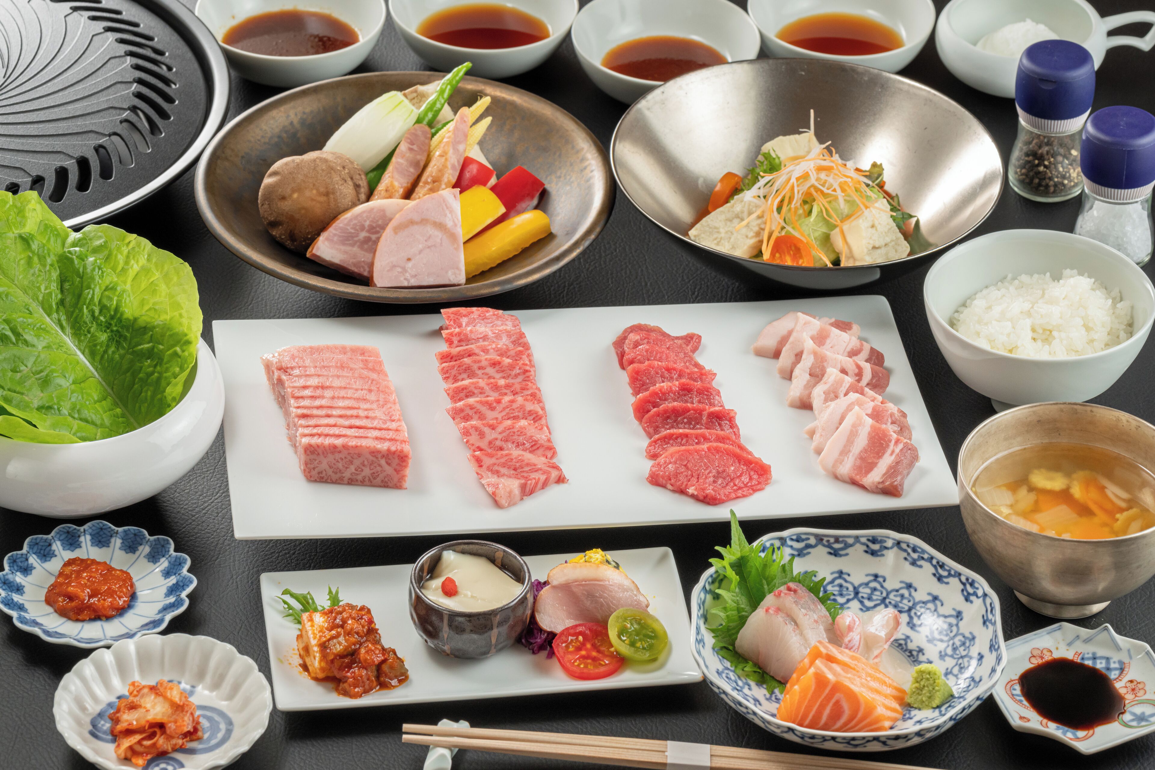 Variedad de platos japoneses, como pescado crudo, verduras y cuencos de arroz.