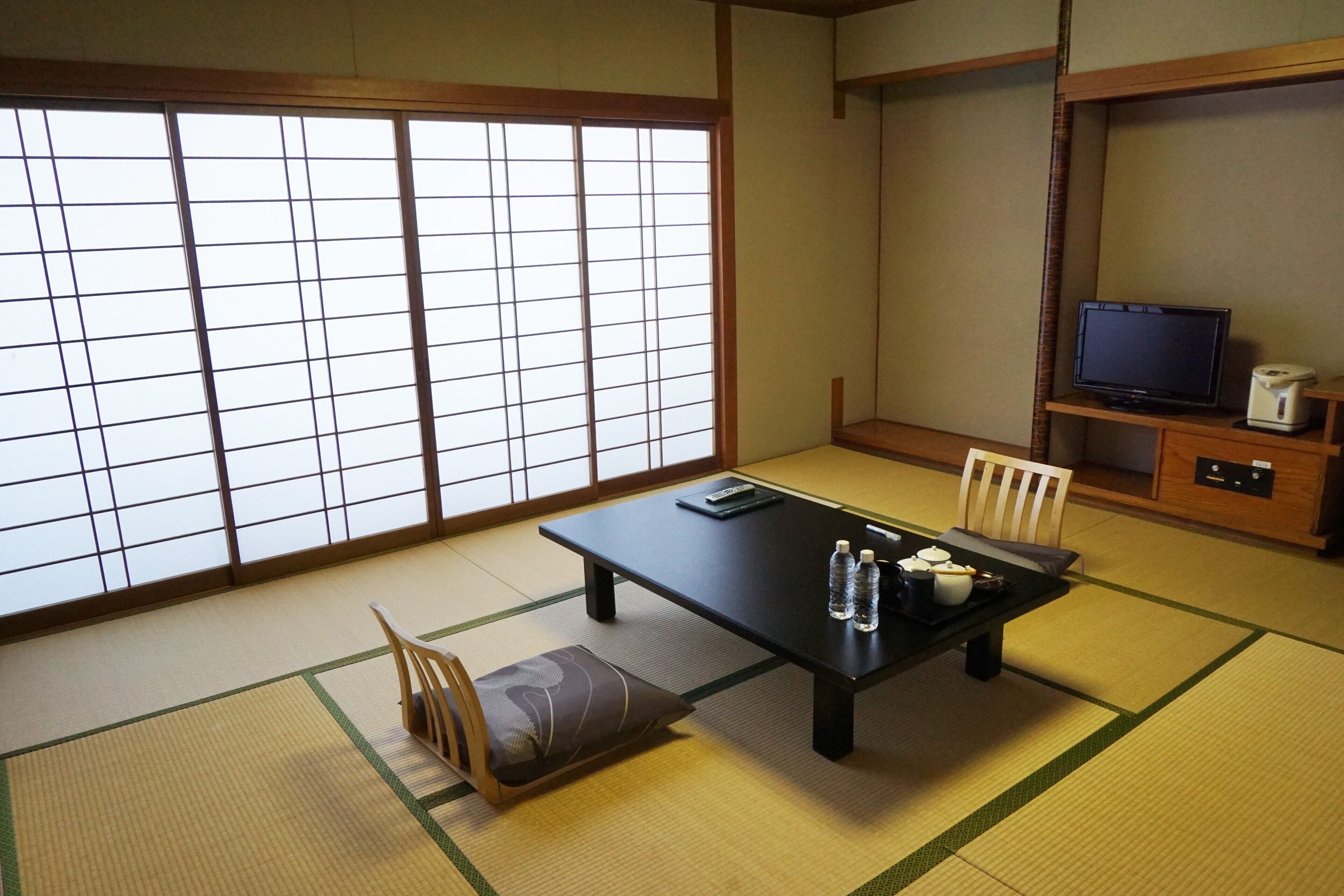 A traditional Japanese room with tatami flooring, a low table with cushions, a television, and a small cabinet.