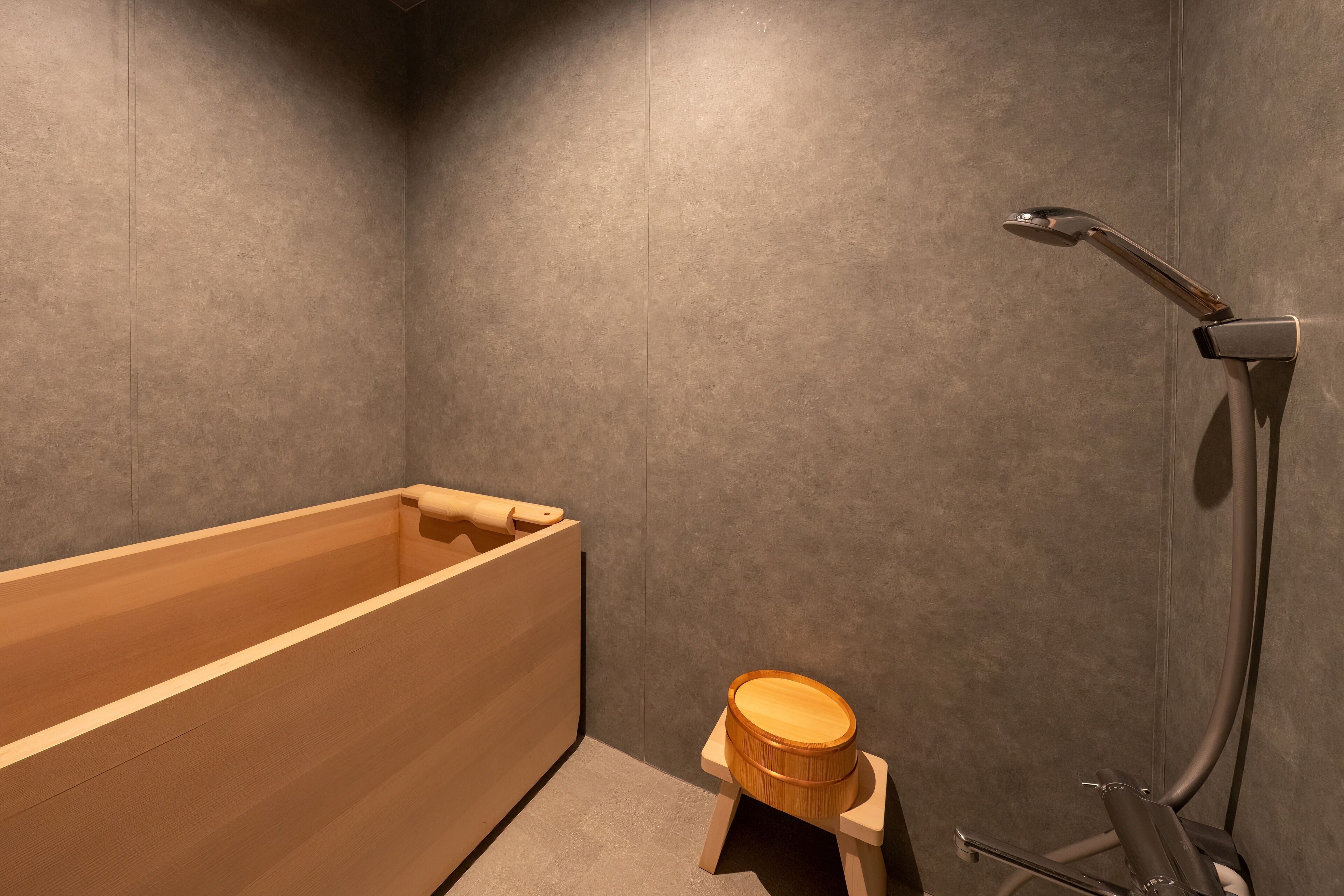 A modern bathroom with a wooden bathtub, a small wooden stool, and a showerhead.