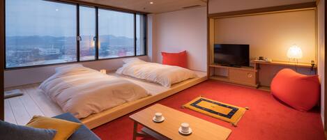 Una habitación de hotel moderna con una cama grande, un televisor, una mesita con tazas y vistas a la ciudad.