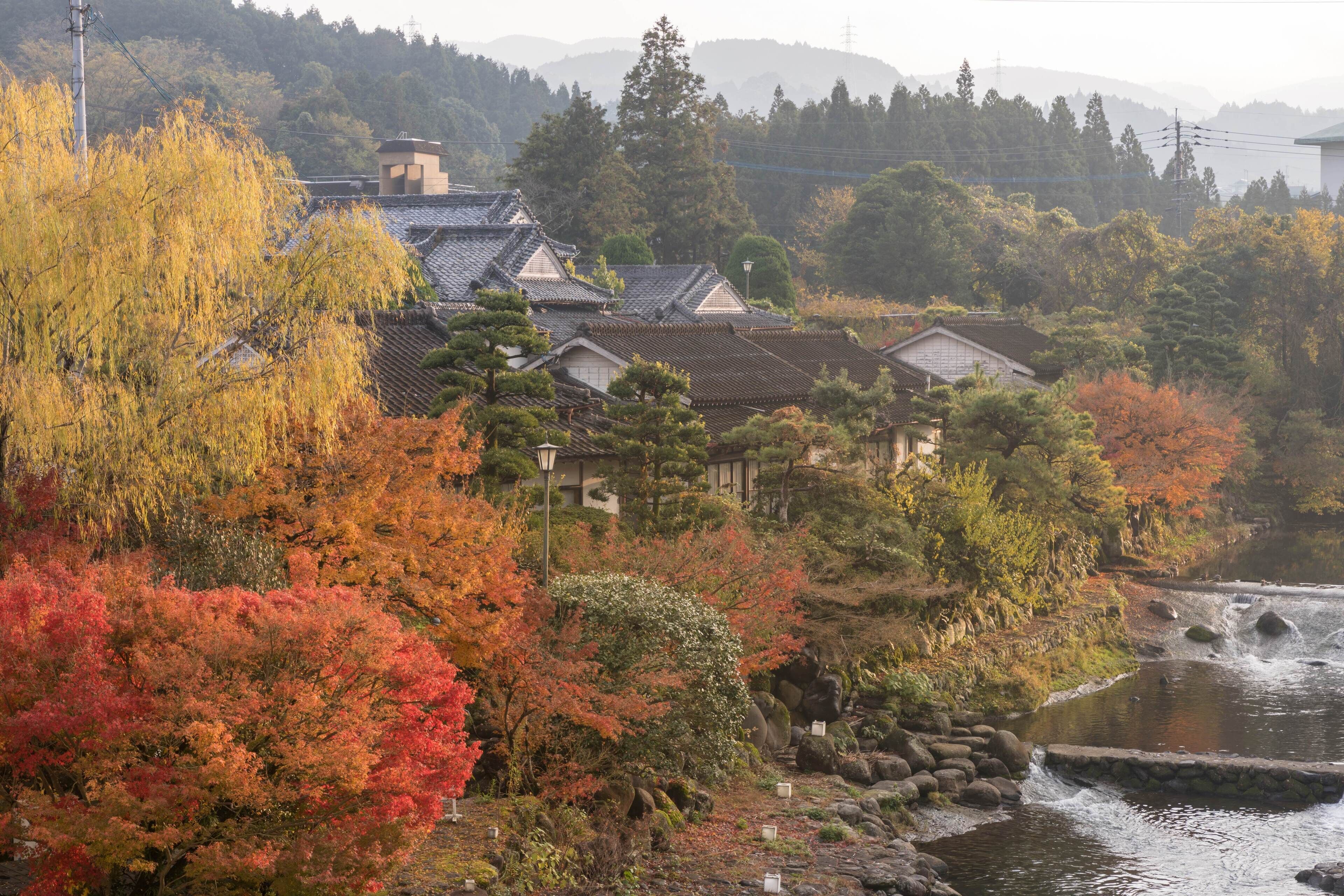 Un village japonais traditionnel, avec ses couleurs automnales, une rivière et ses bâtiments traditionnels.